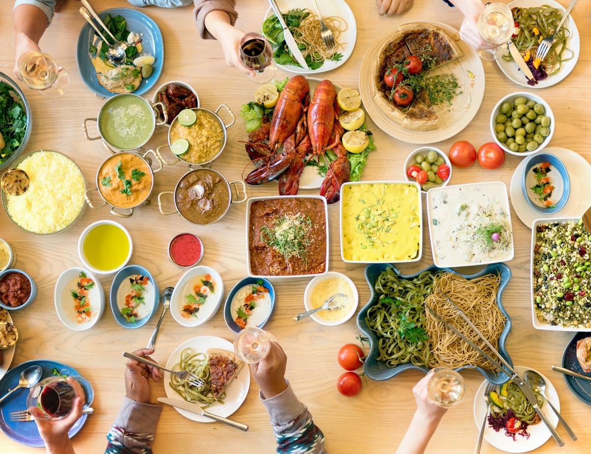 Ein reich gedeckter Tisch mit vielen Vorspeisen (Mezze), von oben fotografiert, mit erhobenen Gläsern.